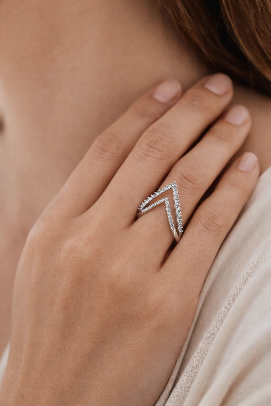Close-up of a hand wearing a silver ring with diamond accents, held against a neutral background.