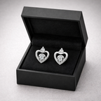 Heart-shaped silver earrings in a black jewelry box on a light gray background