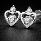 Heart-shaped silver earrings with clear gemstones on a dark background