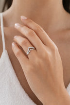 Close-up of a hand wearing a silver ring with a V-shaped design on a blurred background.