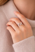 Hand wearing a silver ring with a cross design against a beige background