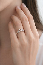 Close-up of a hand wearing a silver ring with a diamond, against a neutral background.