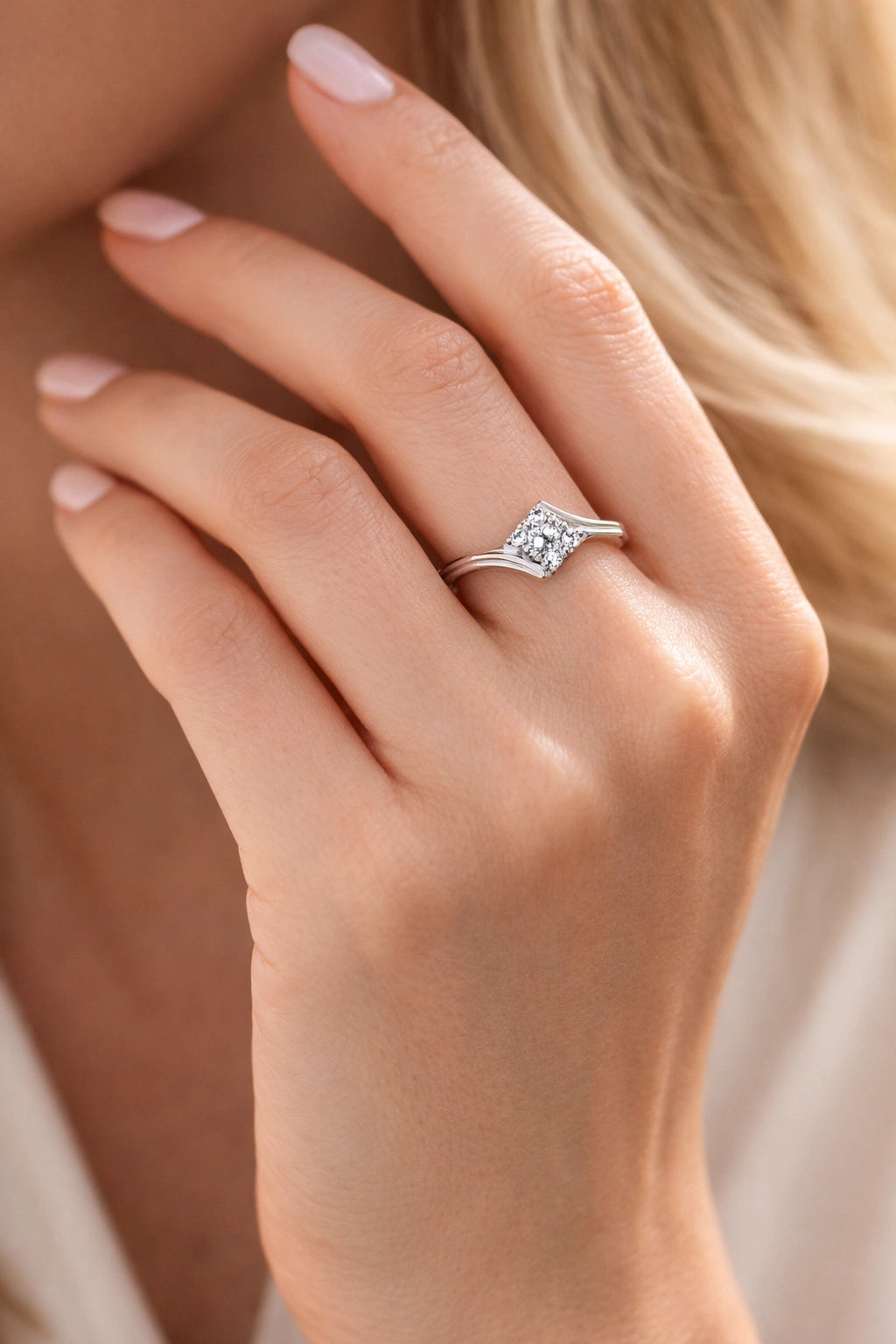 Close-up of a hand wearing a silver ring with a diamond on a blurred background