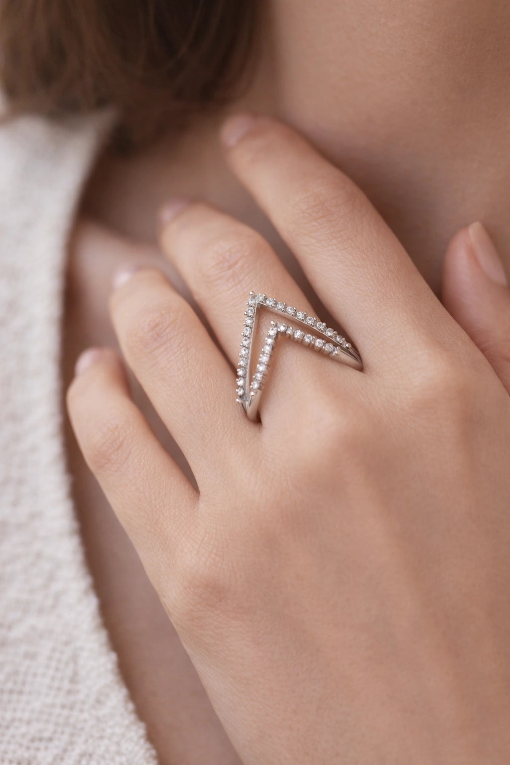 Close-up of a hand wearing a silver chevron-shaped ring on a neutral background