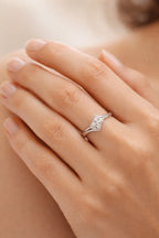 Silver ring with a diamond on a person's finger against a neutral background