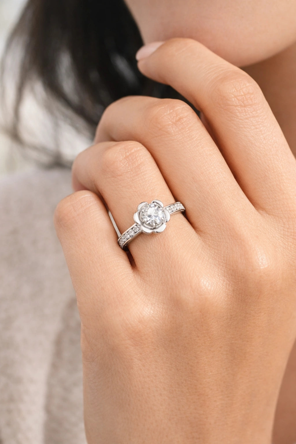 Close-up of a hand wearing a silver ring with a diamond on a neutral background