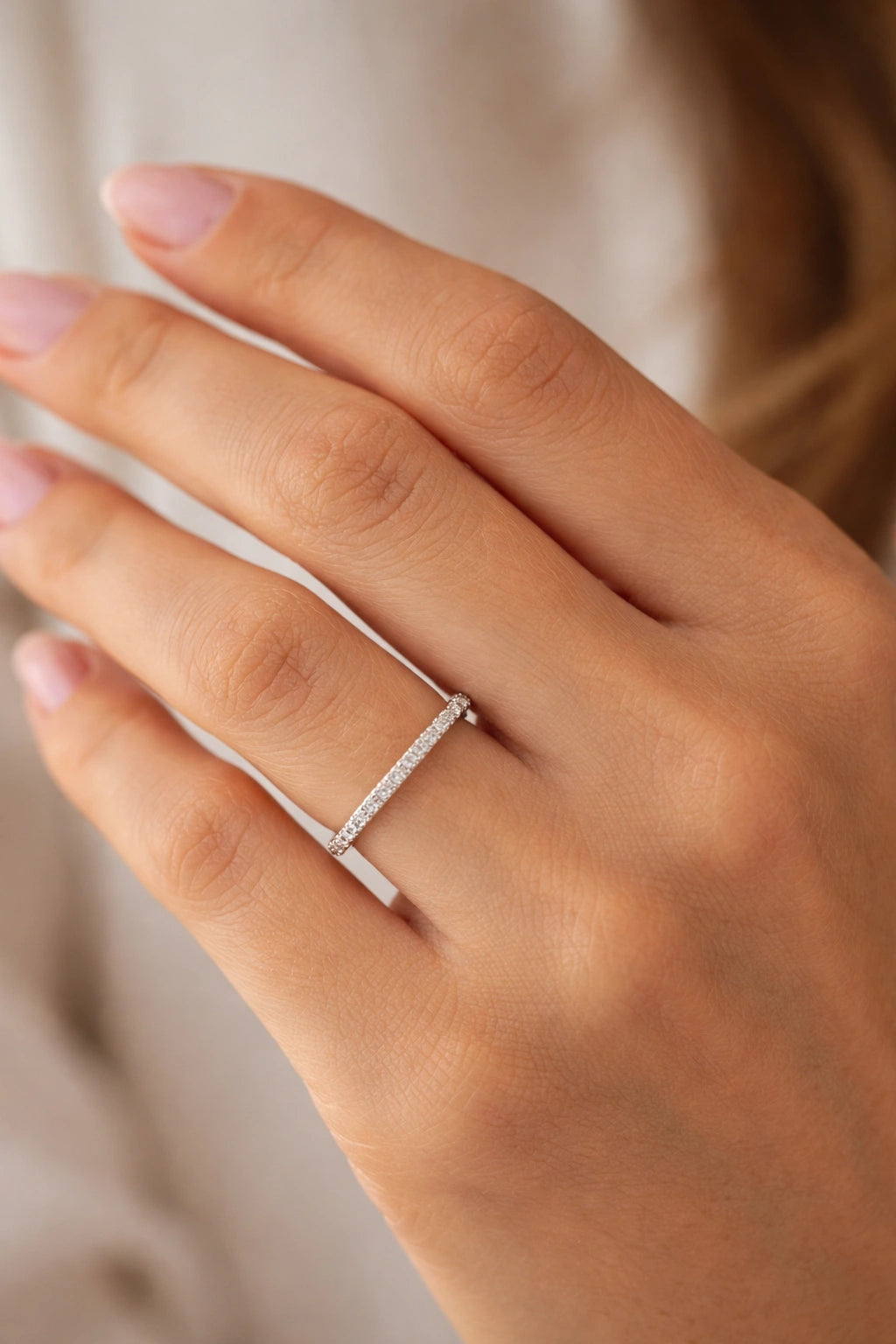 Close-up of a hand wearing a silver ring with small diamonds on a neutral background