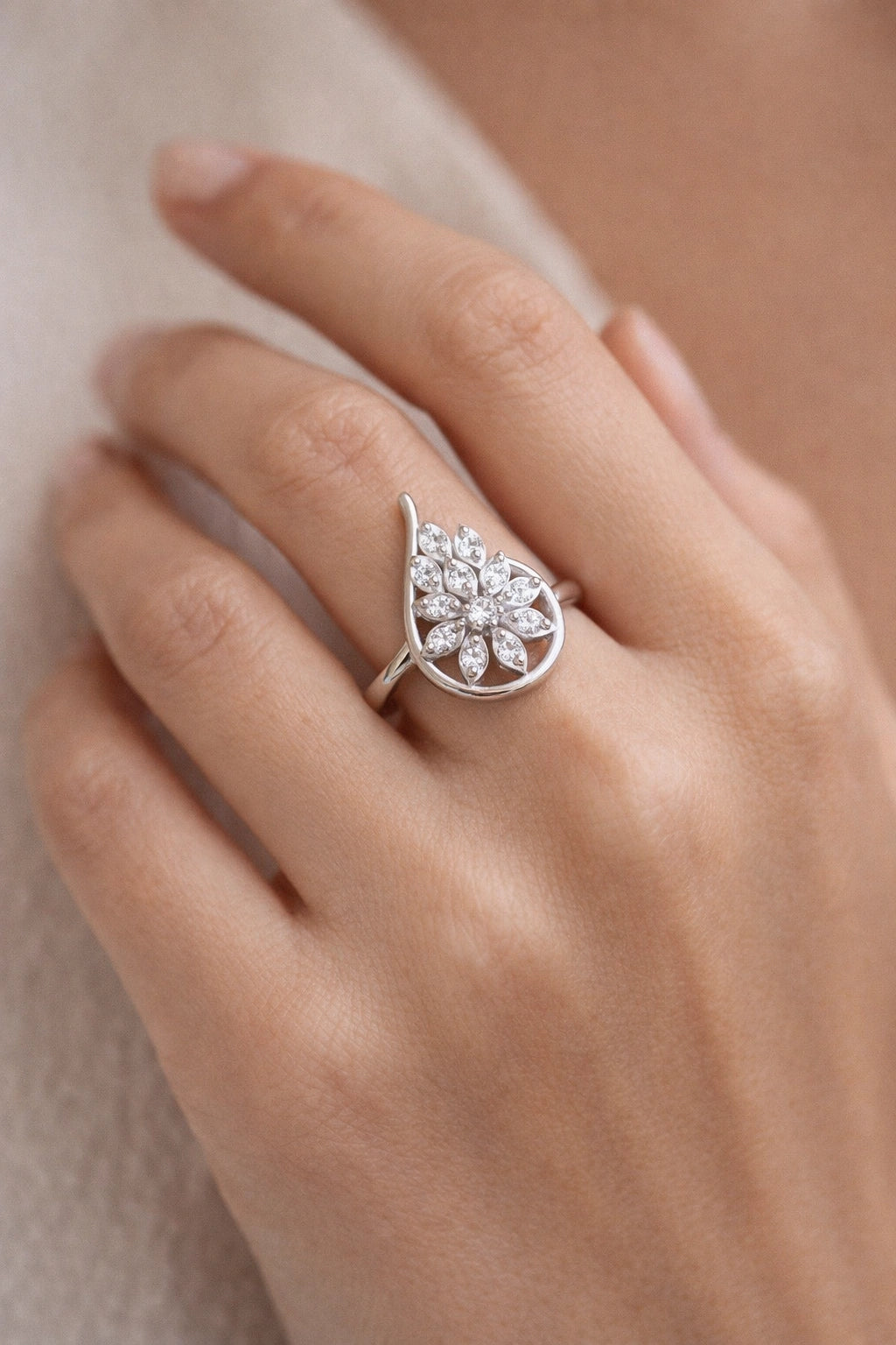 Silver ring with a leaf design on a person's finger against a neutral background